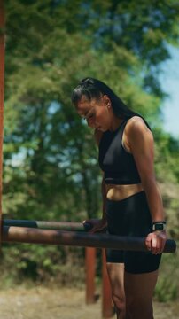 A determined woman engages in an outdoor fitness workout, performing dips on parallel bars. She is focused on her strength training session in a sunny park environment.