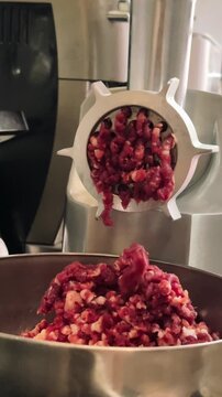 Fresh minced meat coming out of electric meat grinder into stainless steel bowl during homemade meat preparation in home kitchen, 4K.