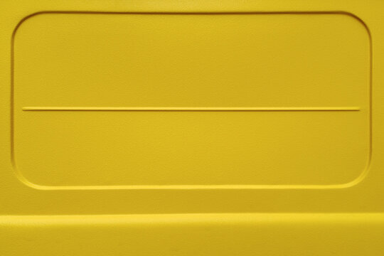 Close-up of a yellow painted metal vehicle body panel with embossed geometric shapes and textured surface. Abstract industrial background with copy space, suitable for design, advertising, packaging a