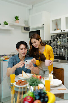 Asian couple watching entertainment on smartphone while having lunch in kitchen room