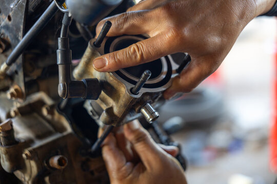 Mechanic hands repairing motorcycle engine carburetor with focused detail and warm tones, showing tools, metal parts, tubing and confident tactile work