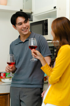 happy Asian couple drinking red wine together in kitchen room