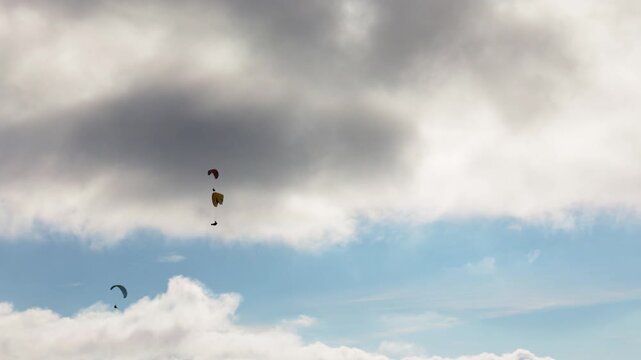 People try paragliding flying with parachutes against clouds