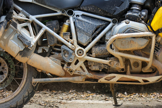 Muddy adventure motorcycle engine and frame close up showing dirt covered suspension, exhaust, skid plate and rear wheel, rugged touring bike worn from off road travel