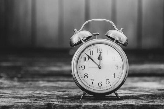 Old vintage alarm clock over blurred wood background, timeline and deadline background idea, black and white filter effect
