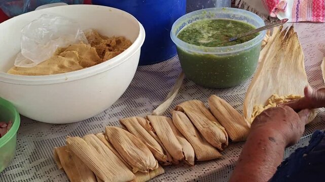 Hands scooping corn masa onto husk leaf to make tamales