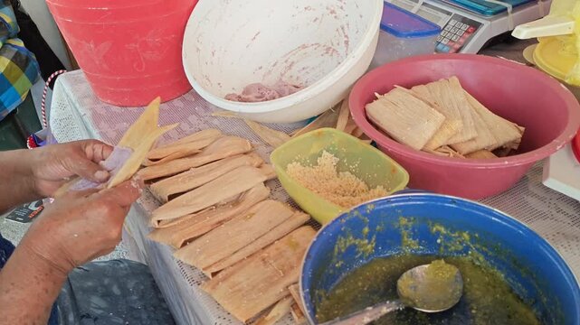 Making tamales adding green sauce and cheese on corn husk