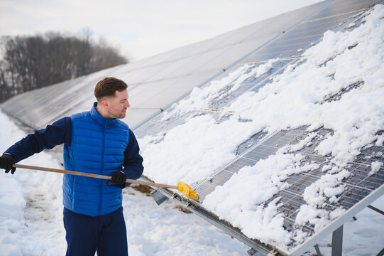 Worker clearing snow from solar panels in winter