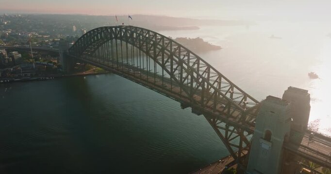 Iconic Sydney Harbour Bridge connecting city districts, bathed in warm morning light, with the city skyline and harbor extending into the distance. Dramatic evening light. Aerial view drone flight