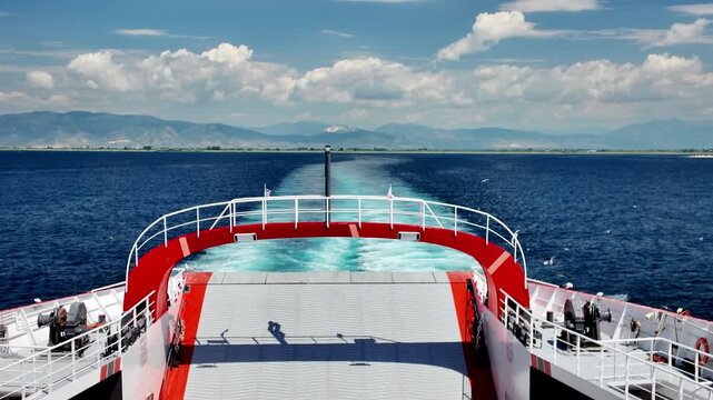 Panoramic view from the ferry deck of the calm sea and mountainous coast, the trail of the ferry against the background of mountains and clouds.