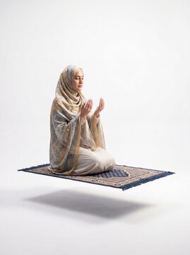 A serene woman wearing a traditional hijab sits in a meditative pose on a floating prayer rug mat.