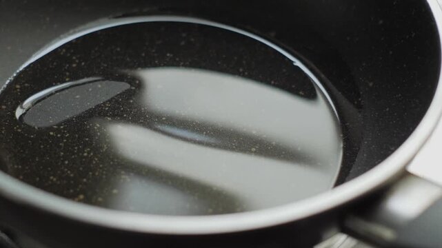 Swirling cooking oil to coat the surface of a black non-stick pan. Concept of food preparation, home cooking, and culinary skills.