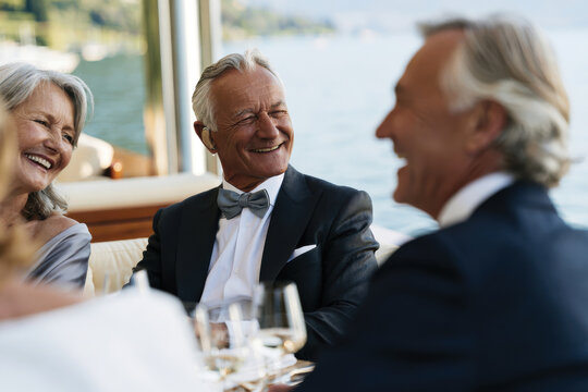 A sophisticated group of older adults enjoys a joyful moment together by the water, capturing an atmosphere of elegance, warmth, and companionship during a sunny outing.