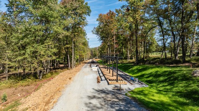 A construction site is seen in a forested area during the day. Workers are preparing the foundation. Trees surround the site, showing the natural landscape. Equipment is set up for building work.