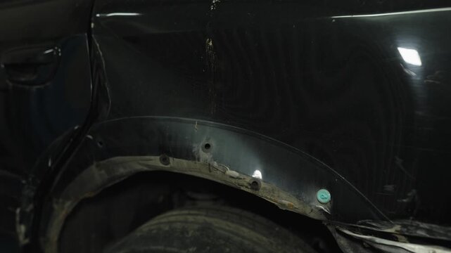 Close-up of a damaged black car rear fender and rusty wheel arch.