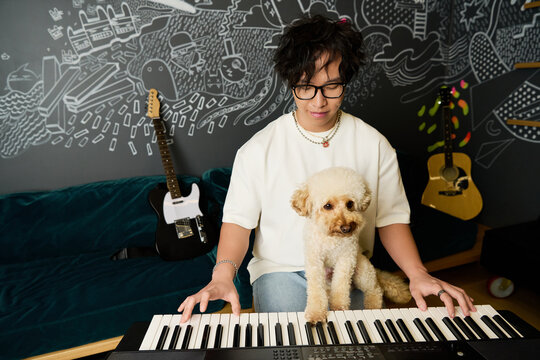 Young Asian man plays keyboard with his adorable dog in a vibrant recording studio