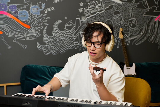 Young Asian man creating music in a vibrant recording studio atmosphere with passion and focus