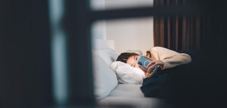 Asian woman sleep on bed at night in bedroom using smartphone social media addiction, dating online with digital communication