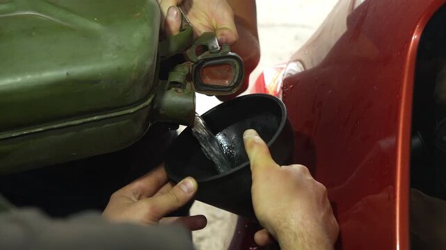 Man pouring fuel from a green jerrycan into a car tank using a funnel.