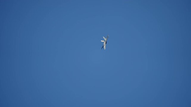 Twin tail fighter jet diving through a maneuver, military aircraft rolling against deep blue sky, combat jet showing its underside at high speed during an air show, filmed in slow motion