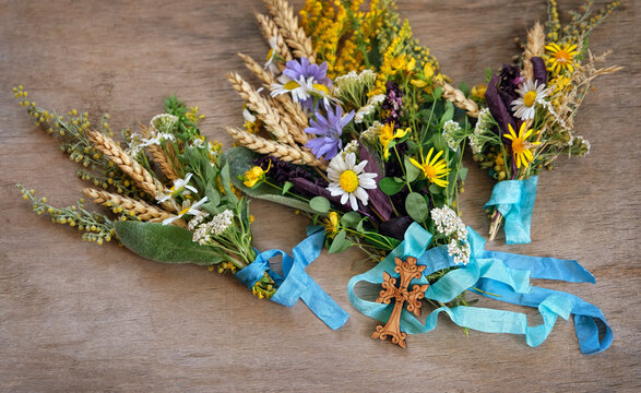 Herbs tied to sacred bouquets with ribbons and wooden cross on rustic table close up. Herbal consecration - traditional customs on August 15, Assumption of Mary day. christian religion ritual
