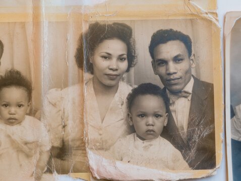 Aged vintage family portrait with worn torn edges showing a couple and two young children for genealogy and historical memory concepts