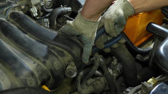 Mechanic hands in gloves using pliers to repair car engine components.