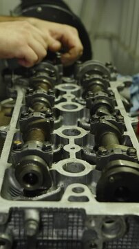 Mechanic hands repairing and adjusting camshafts on an open car engine block.