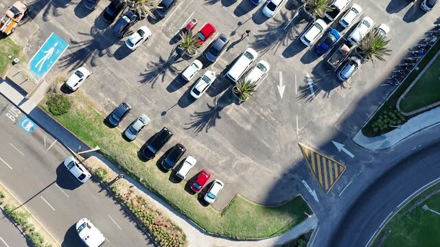 Top down aerial drone footage flying over a coastal skatepark, palm tree parking area and urban streets in Punta del Este, Uruguay. Modern city infrastructure captured from directly above on a sunny d