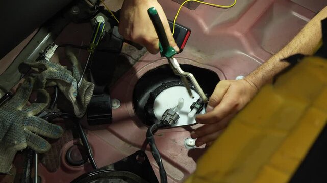 Mechanic hands replacing car fuel pump module under rear seat.