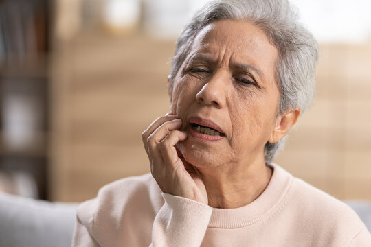 Senior woman suffering from toothache while touching painful cheek at home. Dental pain, oral health, sensitive teeth, gum problem, healthcare, discomfort and healthy aging concept.