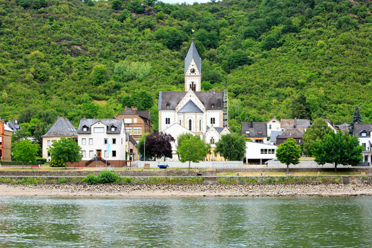 View of white-washed pretty village church and cottages seen from a river cruise along the Rhine River in Germany
