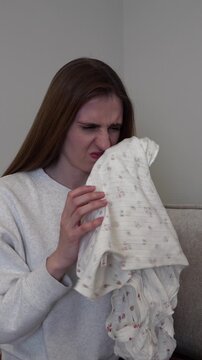 Young woman smells a piece of clothing and reacts with disgust after noticing an unpleasant odor. Ideal for laundry, fabric care, household hygiene, dirty clothes and home cleaning concepts.