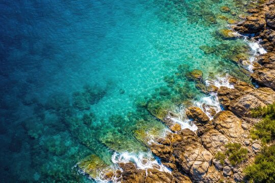 Clear Turquoise Water Breaking on Rocky Shoreline Under Bright Sunlight