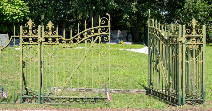 An ornate pair of open weathered wrought-iron cemetery gates