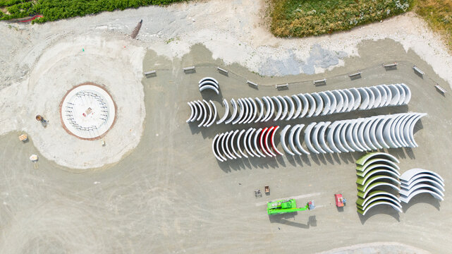 Construction site, preparation for building wind turbine farm, concrete tower section, foundation area, rows of curved segments, gravel ground in forest, Germany