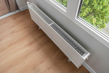 Naklejka premium A modern white heating radiator is mounted under a window in a bright room with light wooden flooring.