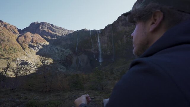 Close up of a hiker eating, with the Casta&ntilde;o Overa glacier and cascading waterfalls in the blurred background, located in Nahuel Huapi National Park, Argentina.