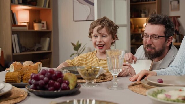 Caucasian child expressing excitement and laughing while sitting with Caucasian father at dinner table. Clip for family lifestyle and healthy food advertisements