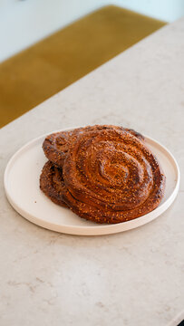 Sweet Cinnamon Swirl: Two golden brown, freshly baked cinnamon swirl pastries rest on a minimalist white plate, hinting at a delightful morning treat or a satisfying afternoon snack.