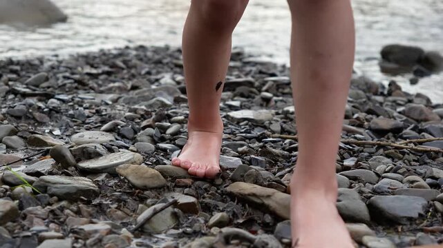 Caucasian child boy walks with his feet on the shore with stones. Children's legs and feet. Vacation, leisure, rest in a mountain river. Happy childhood