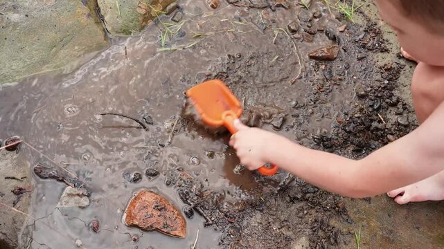 Caucasian child boy playing with a shovel in the mud on the stone bank of the river. Vacation, leisure, rest in a mountain river. Happy childhood