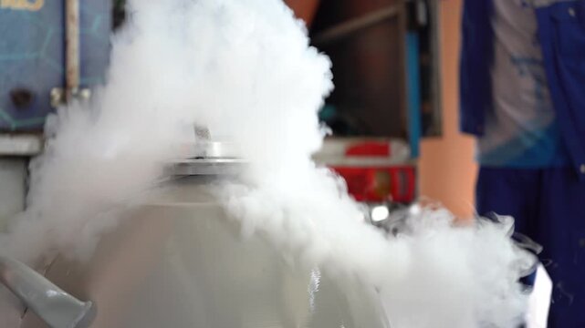 A large industrial container emits thick cold nitrogen vapor in a workshop setting.