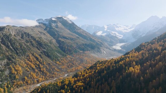 Aerial drone video of a colorful autumn forest in a mountain valley. Golden sun rays and fog over misty woods and mountain peaks at sunrise.