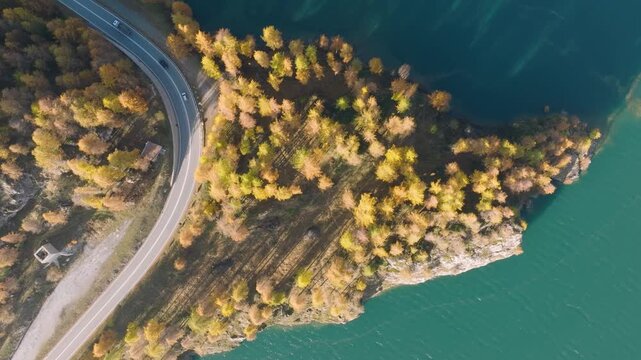 Aerial drone view of an asphalt road with cars driving near a lake surrounded by autumn forest. Scenic fall landscape for travel background and transportation. 