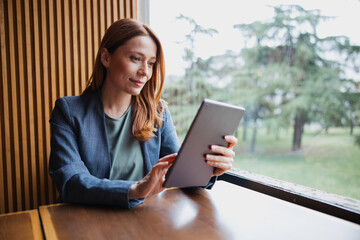 Attractive female professional working on a tablet computer while sitting in a coffee shop © Novak