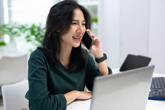 Young businesswoman talking on smartphone while working in modern office. Professional communication, customer service, remote work, and business productivity concept.
