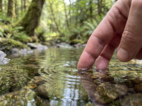 Hand dipping fingers into clear cool flowing water of river