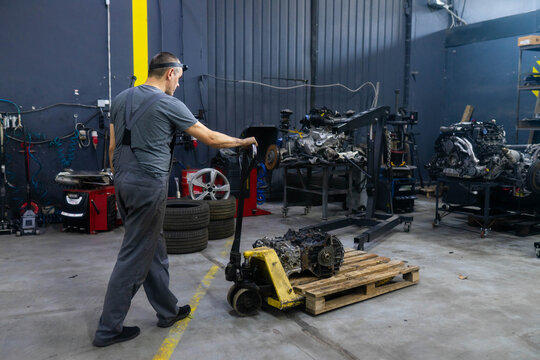 Strong man auto service worker moves heavy metal car engine using forklift. Experienced male mechanic transports engine for detailed repair