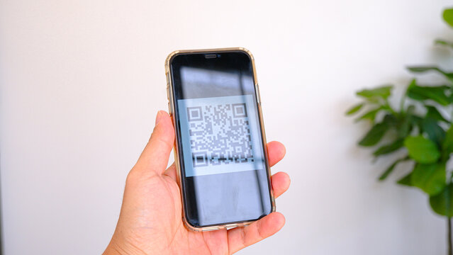 Hand holding smartphone displaying QR code on screen for digital payment or scanning against white wall background